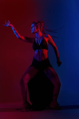 Siyah giyimli ve örgülü saçlı kadın mavi ve kırmızı bir B 'de dans ediyor.