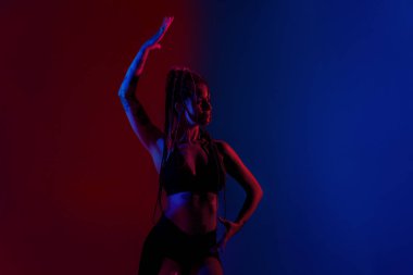 Siyah giyimli ve örgülü saçlı kadın mavi ve kırmızı bir B 'de dans ediyor.