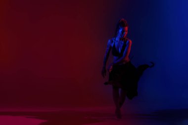 Siyah giyimli ve örgülü saçlı kadın mavi ve kırmızı bir B 'de dans ediyor.