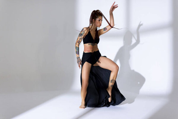 Black dressed and braided hair woman with tattoos dancing on a w