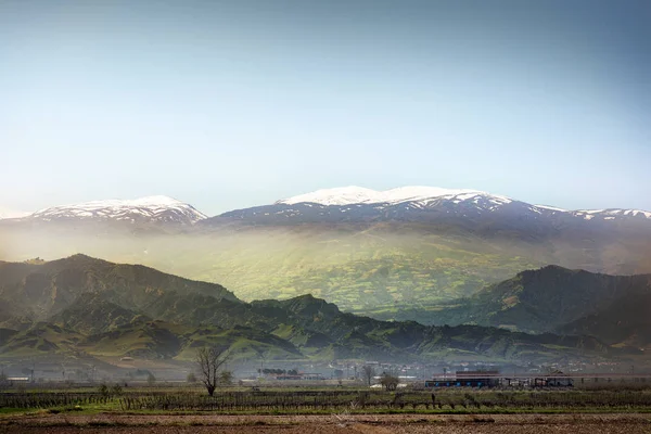 Вспаханное поле и снежные горы на фоне пейзажа . — стоковое фото
