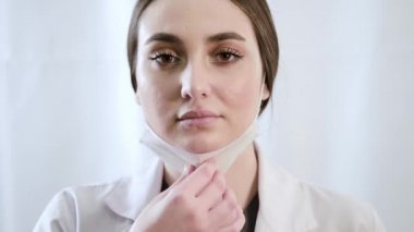 Maske takan ve beyaz arka plandaki kameraya bakan bir kadın doktorun portresi.