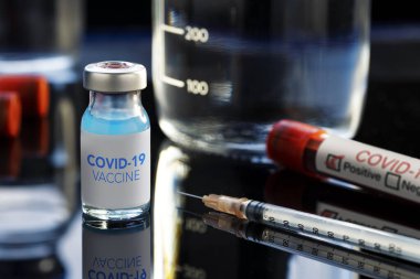 Covid-19 yazılı aşı şişesinde mavi bir sıvı, şırınga ve kan örneği var..