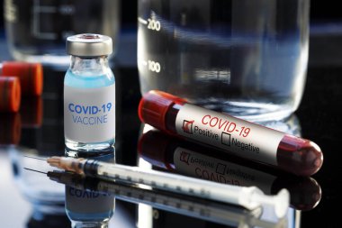 Covid-19 yazılı aşı şişesinde mavi bir sıvı, şırınga ve kan örneği var..