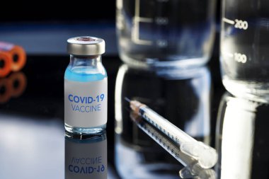 Covid-19 yazılı aşı şişesinde mavi bir sıvı ve şırınga var..