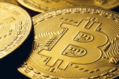 Yüksek kontrastlı siyah arkaplandaki altın renkli bitcoin paralar.