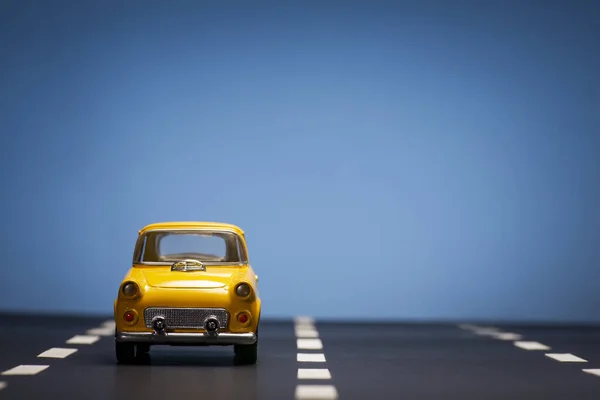 Vooraanzicht Van Een Gele Speelgoedauto Een Blauwe Achtergrond Een Asfaltweg — Stockfoto