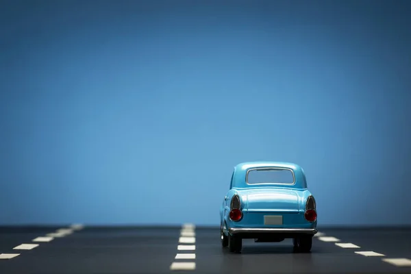 Achteraanzicht Van Een Blauwe Speelgoedauto Een Blauwe Achtergrond Een Asfaltweg — Stockfoto