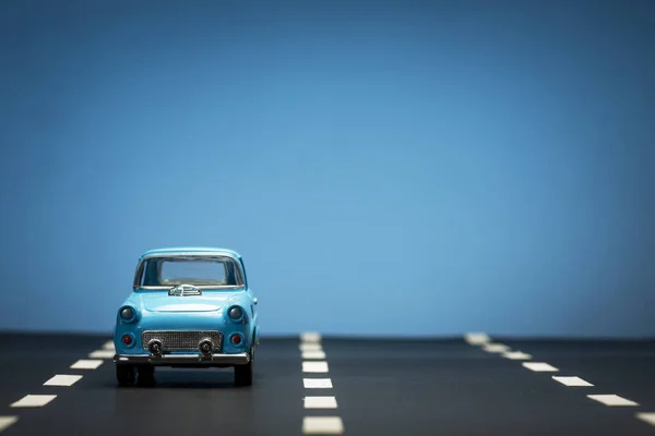 Vooraanzicht Van Een Blauwe Speelgoedauto Een Asfaltweg Een Blauwe Achtergrond — Stockfoto