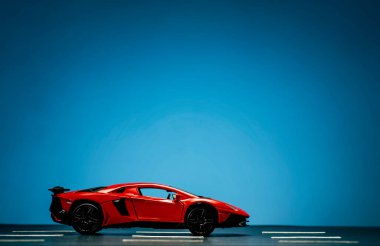 Asfalt ve mavi arka planda yol şeritleri olan kırmızı bir spor arabanın yan görüntüsü.