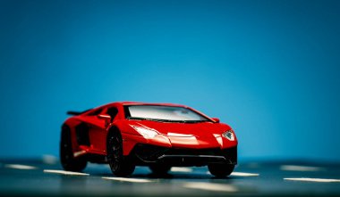 Asfalt ve mavi arka planda yol şeritleri olan kırmızı bir spor arabanın ön görüntüsü.