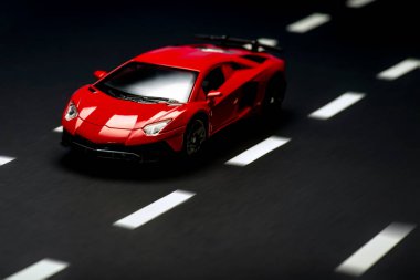 Yol şeritli asfalt bir arka planda kırmızı bir spor arabanın ön görüntüsü.