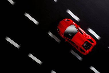 Yol şeritleri olan asfalt bir zeminde kırmızı bir spor arabanın üst görüntüsü.
