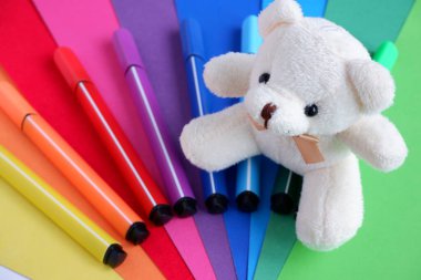 Gökkuşağı şeklinde çok renkli güzel bir karton ve gökkuşağı şeklinde çok renkli işaretler ve peluş bir oyuncak ayı bej rengi. Okul malzemeleri. Her türlü reklam geçmişi ve tebrik kartları için uygundur.