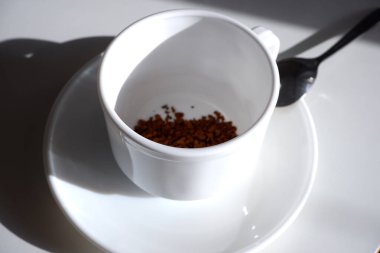 Bir fincan çay tabağı, hazır kahve ve beyaz arka planda bir kaşık. Rengi beyaz. Seramik.