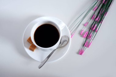 Çay seti: fincan, çay tabağı ve kaşık. İki parça şeker. Çiçeklerle beyaz bir arkaplanda