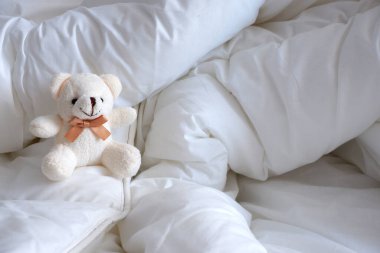 Yumuşak oyuncak ayı, beyaz renkli beyaz çarşaf üzerinde oturan.