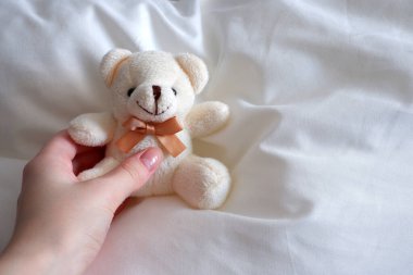 Çarşafların üzerinde oturan yumuşak kutup ayısı. Yumuşak bir oyuncağı tutarken.