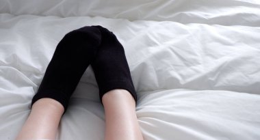 Siyah çoraplı ayaklar, yumuşak, beyaz bir battaniyenin altında.