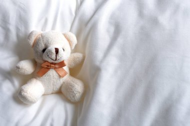 Yumuşak bej bir ayı, yumuşak beyaz bir yatakta oturuyor. Çocuk oyuncağı..
