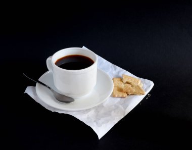 Siyah arka planda bir fincan sade kahve ve kurabiye. Model ve reklam geçmişleri için uygun.