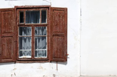 Beyaz bir duvarda ahşap panjurları olan eski bir pencere.