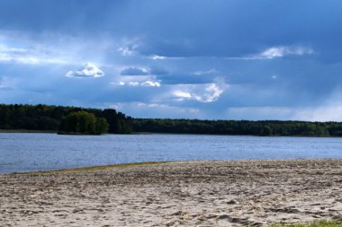 Kumsal ve bulutlar güneşten parlıyor yeşil bir orman ve mavi bir nehir üzerinde