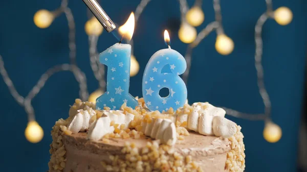 Tarta de cumpleaños con vela de 16 números sobre fondo azul prendida fuego por encendedor. Primer plano —  Fotos de Stock