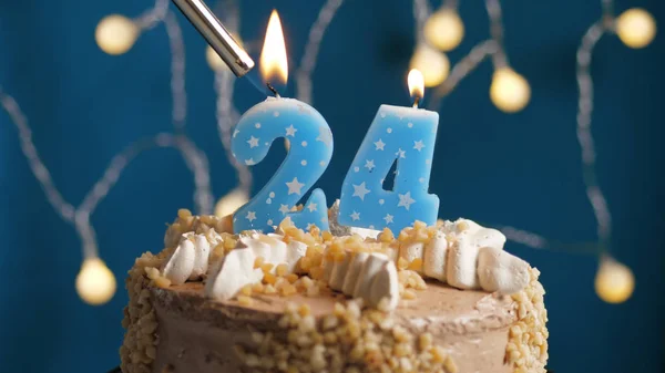 Birthday cake with 24 number candle on blue backgraund set on fire by lighter. Close-up