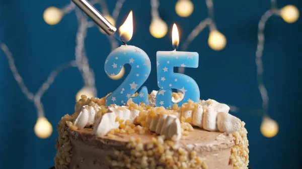 Bolo de aniversário com vela número 25 em backgraund azul incendiado por isqueiro. Close-up — Fotografia de Stock