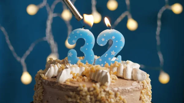Bolo de aniversário com 32 vela número em backgraund azul incendiado por isqueiro. Close-up — Fotografia de Stock