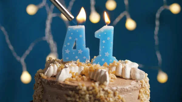 Birthday cake with 41 number candle on blue backgraund set on fire by lighter. Close-up