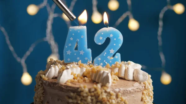 Birthday cake with 42 number candle on blue backgraund set on fire by lighter. Close-up — Stock Photo, Image