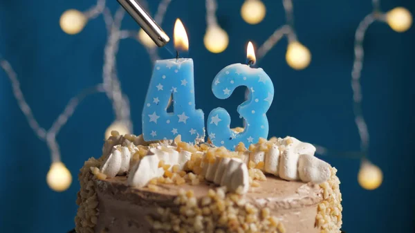 Tort urodzinowy z 43 świecą numer na niebieskim tle podpalony zapalniczką. Zbliżenie — Zdjęcie stockowe