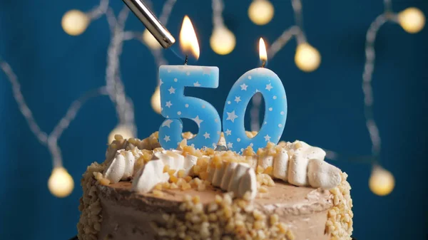 Birthday cake with 50 number candle on blue backgraund set on fire by lighter. Close-up — Stock Photo, Image