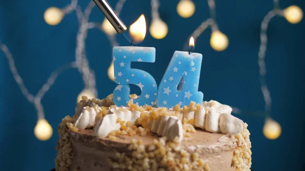 Verjaardagstaart met 54-cijferige kaars op blauwe achtergrond in brand gestoken door aansteker. Close-up — Stockfoto