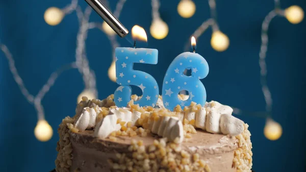 Verjaardagstaart met 56-cijferige kaars op blauwe achtergrond in brand gestoken door aansteker. Close-up — Stockfoto