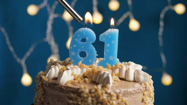 Pastel de cumpleaños con 61 número de vela en el fondo azul incendiado por el encendedor. Primer plano —  Fotos de Stock