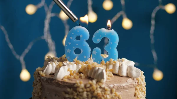 Gâteau d'anniversaire avec bougie 63 chiffres sur fond bleu mis le feu par briquet. Gros plan — Photo