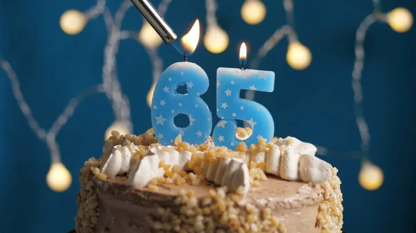 Gâteau d'anniversaire avec bougie à 65 chiffres sur fond bleu mis le feu par briquet. Gros plan — Photo