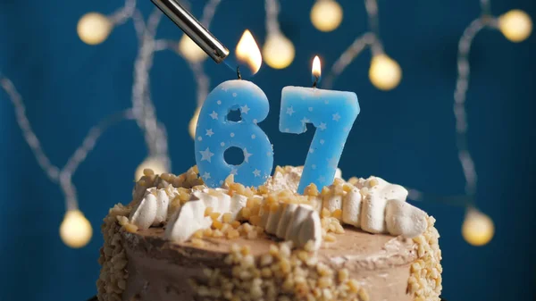 Tarta de cumpleaños con una vela de 67 números en el fondo azul incendiada por un encendedor. Primer plano —  Fotos de Stock