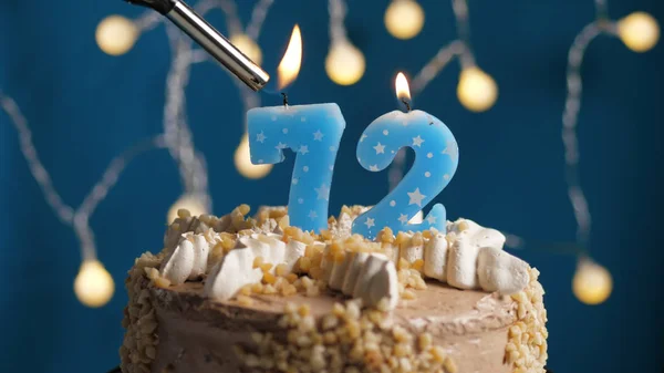 Birthday cake with 72 number candle on blue backgraund set on fire by lighter. Close-up