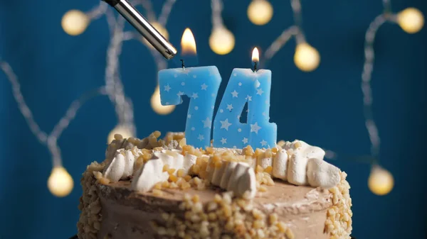 Birthday cake with 74 number candle on blue backgraund set on fire by lighter. Close-up