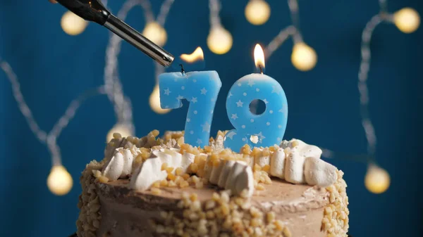 Birthday cake with 79 number candle on blue backgraund set on fire by lighter. Close-up