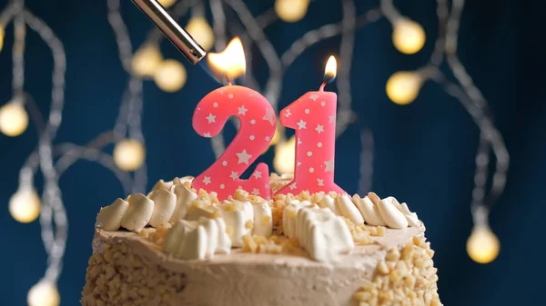 Birthday cake with 21 number candle on blue backgraund set on fire by lighter. Close-up view