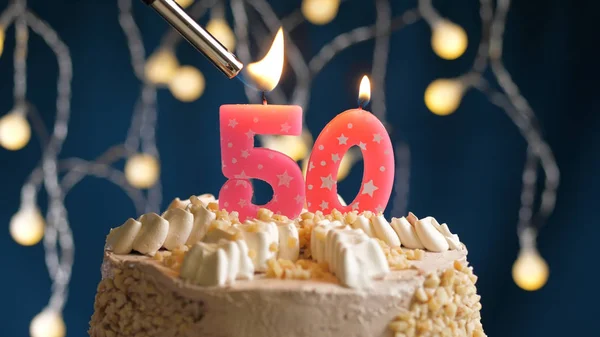 Urodzinowy tort z 50 cyframi świecy na niebieskim tle podpalony zapalniczką. Widok z bliska — Zdjęcie stockowe