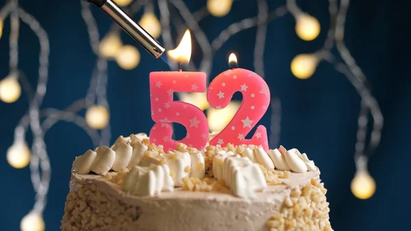 Birthday cake with 52 number candle on blue backgraund set on fire by lighter. Close-up view
