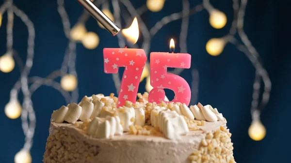 Tarta de cumpleaños con vela de 75 números en el fondo azul prendida fuego por el encendedor. Vista de primer plano —  Fotos de Stock