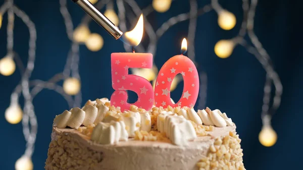 Birthday cake with 50 number candle on blue backgraund set on fire by lighter. Close-up view Stock Image