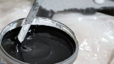 Black concentrated color paint is mixed with white paint in bucket. Wall painting concept. Close-up clipart